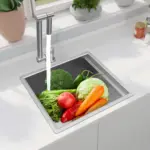 Fresh vegetables in a kitchen sink with running water.