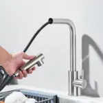 Hand holding a detachable spray nozzle from a modern kitchen faucet.