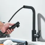 Person using a black pull-out kitchen faucet over a sink.