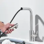 Person using a detachable kitchen faucet sprayer over a sink.