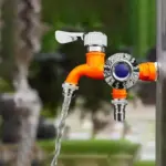 Bright orange outdoor water faucet with flowing water.